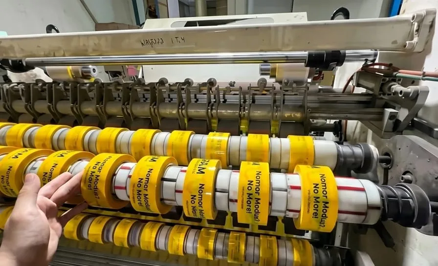 Proses printing custom logo pada lakban kuning di mesin produksi Harmony